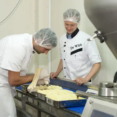 Twee vakbekwame medewerkers vers bereiden deeg op een productielijn in een bakkerijomgeving
