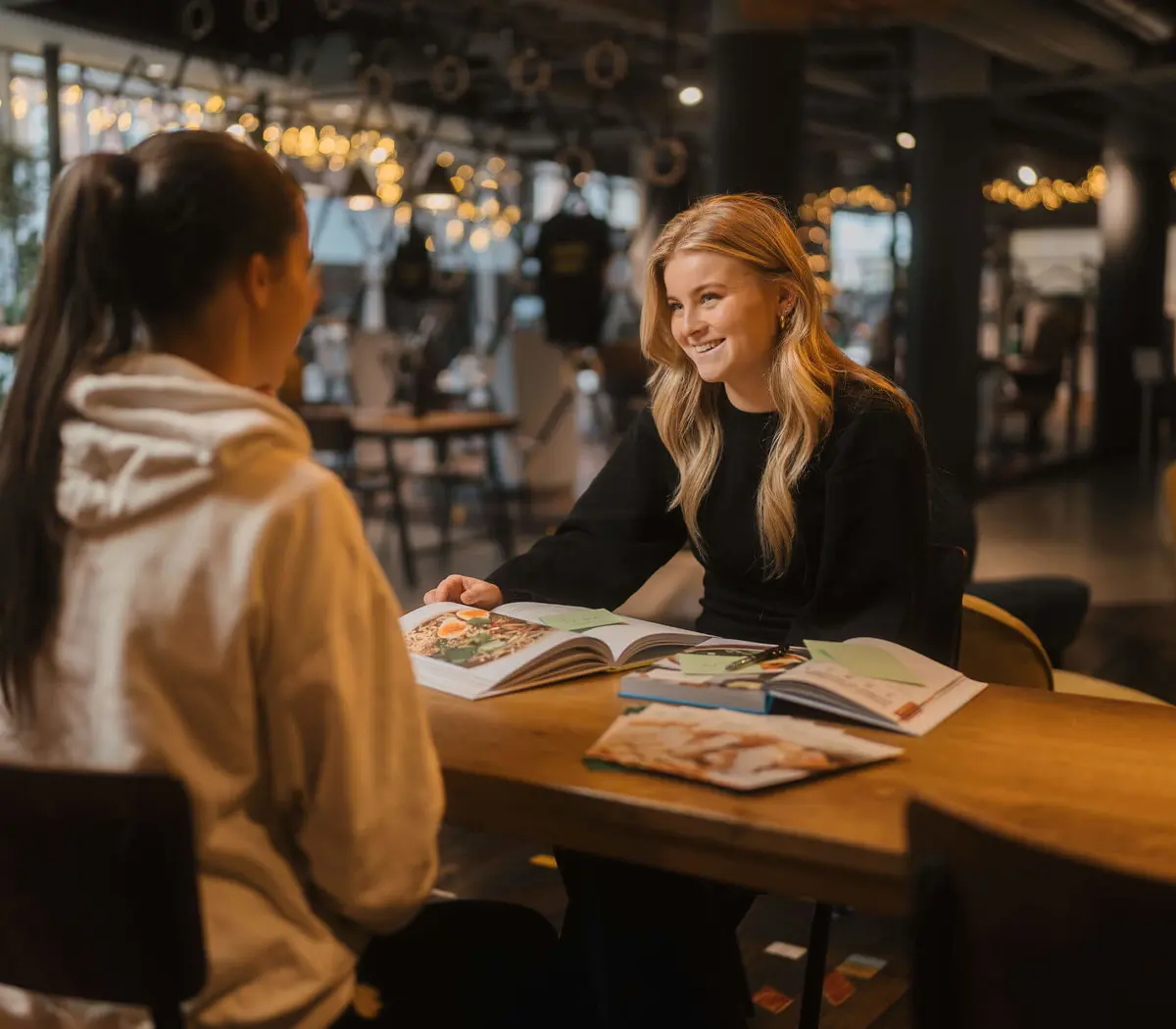 Twee studentes in gesprek aan tafel met open studieboeken over voeding en leefstijladvies.