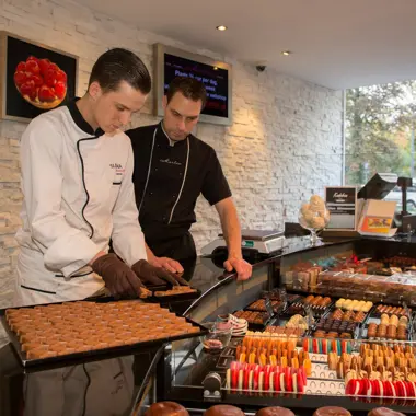 Twee professionals bereiden en rangschikken verschillende gebakjes in een landelijke bakkerijwinkel.