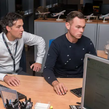 Twee studenten transport en logistiek volgen een les over luchtvrachtplanning aan een bureau met computers