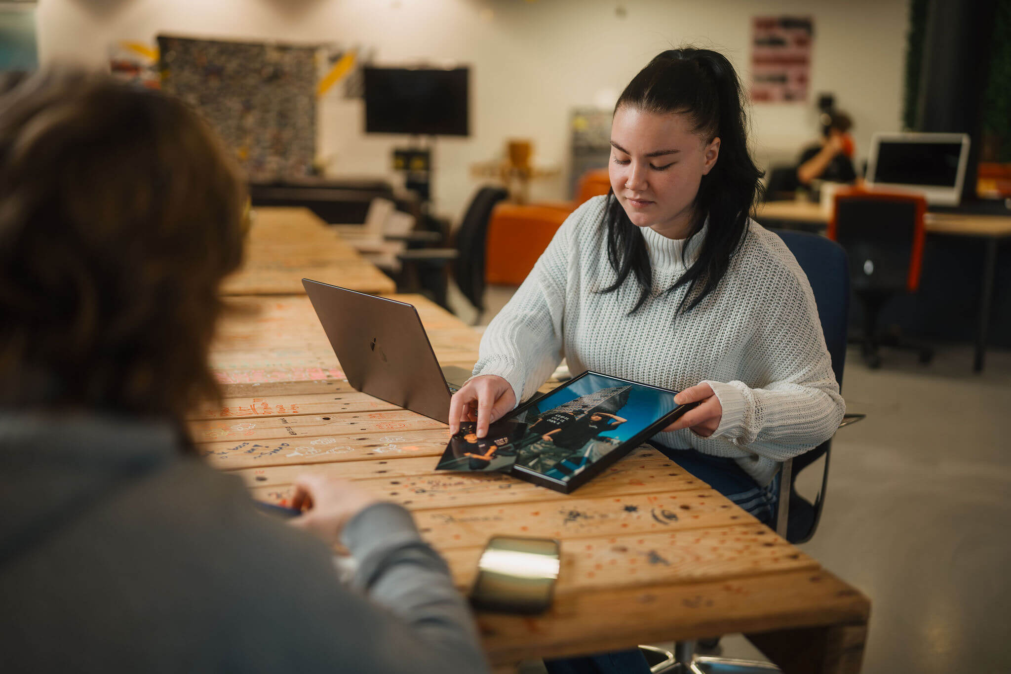 Student bespreekt portfolio met begeleider aan tafel in een leeromgeving gericht op creatief vakmanschap.