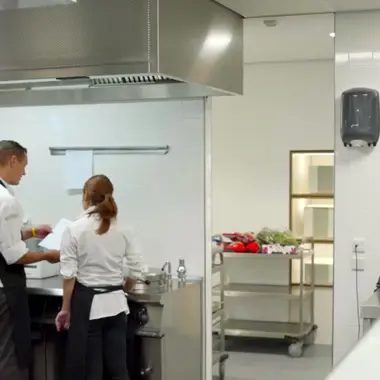 Twee horecamedewerkers bespreken werkzaamheden in een professionele keukenomgeving.