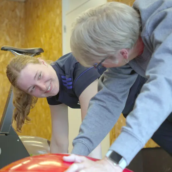 Begeleider ondersteunt deelnemer tijdens oefening op roeimachine in sportomgeving