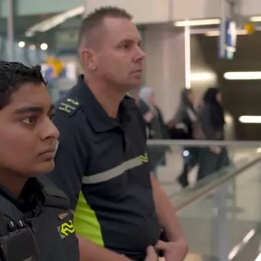 Twee mbo-studenten in veiligheidshulpverleningskleding staan alert in een publieke ruimte.