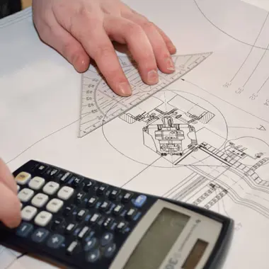 Een tekenaar werkt met een rekenmachine en technische tekening voor werktuigkundige installaties.