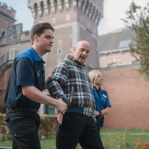 Beveiligers begeleiden een bezoeker buiten een historisch kasteel met toezicht en ondersteuning