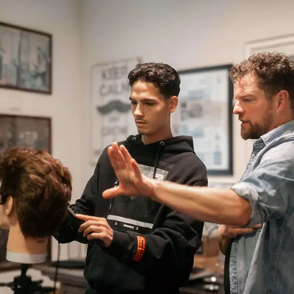 Student en docent oefenen kappersvaardigheden met een oefenhoofd in een kapsalonomgeving