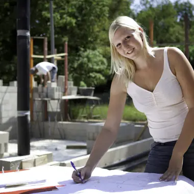 Een uitvoerder bekijkt bouwtekeningen en maakt notities op een bouwplaats met muren in opbouw.