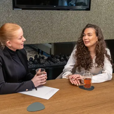Twee personen overleggen aan tafel met een drankje bij een gesprek over retail en winkelmanagement.