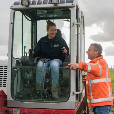 Leerling krijgt instructies over grondverzetmachine van instructeur op bouwlocatie voor wegen en infrastructuur.