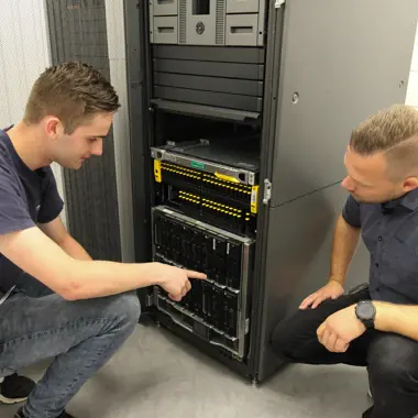 Twee studenten werken samen aan het oplossen van een netwerkprobleem in een serverruimte.