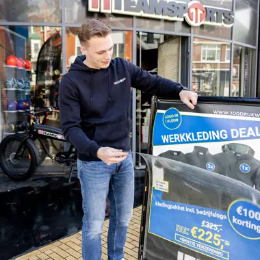 Student die reclamebord met werkkledingdeal bekijkt bij sportwinkel in winkelstraat