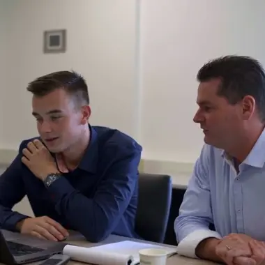 Twee technische studenten bespreken een project op een laptop in een lesruimte gericht op installaties.