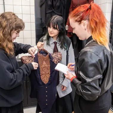 Ontwerper en begeleider bekijken samen kledingstuk tijdens modeopleiding in atelieromgeving