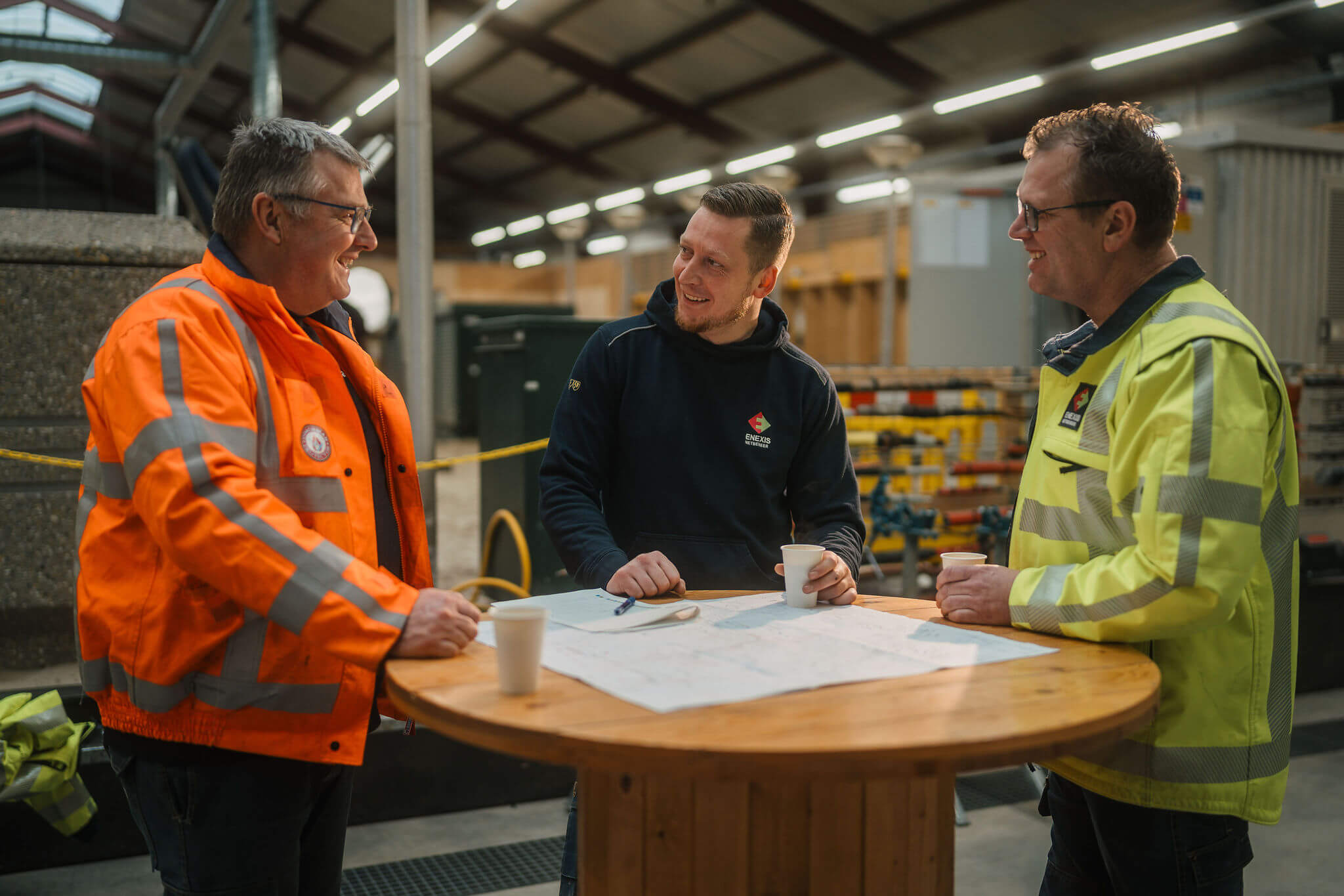 Technische medewerkers bespreken een plan voor elektrotechnische installaties in een werkplaatsomgeving