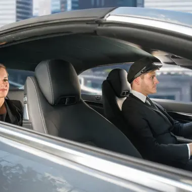 Chauffeur achter het stuur van een auto met een passagier op de achterbank, in een situatie die transport en mobiliteit illustreert.