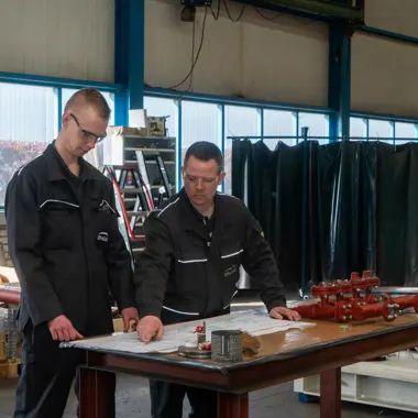 Twee techniekleerlingen bestuderen een technisch schema in een praktijkruimte voor installatietechniek.