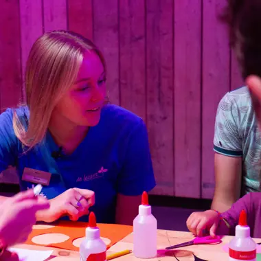 Medewerker begeleidt kinderen bij knutselactiviteiten met lijm en papier tijdens recreatieprogramma