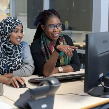Twee studenten werken samen aan een zakelijke taak achter een computerscherm in een kantooromgeving