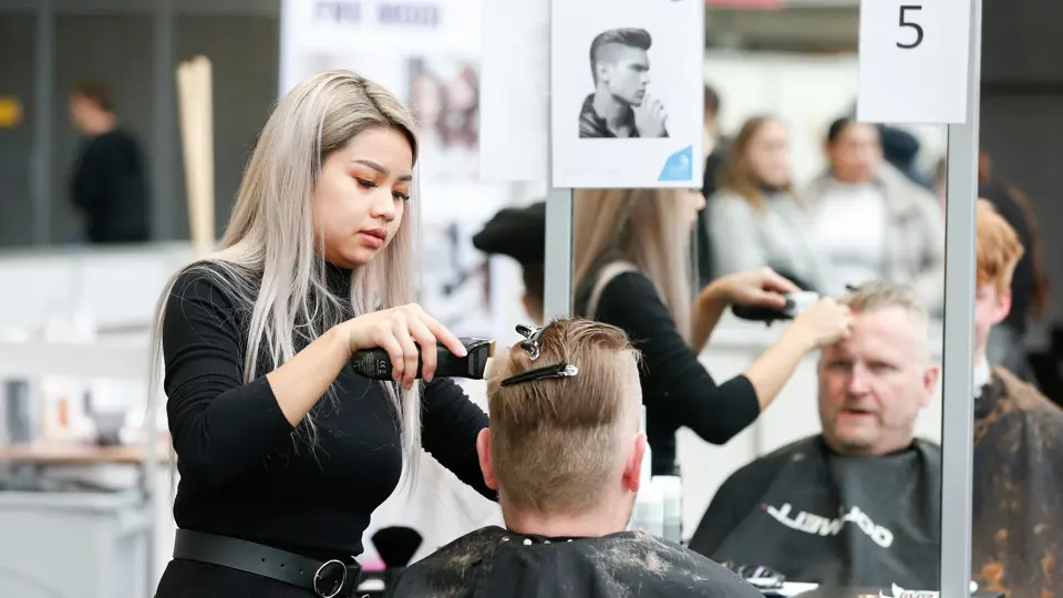 Barbiersstudent oefent knippen en stylen van haar in een salonsituatie met spiegel en klant.