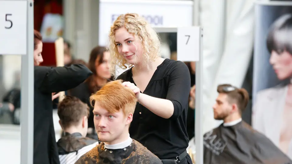 Leerling knipt en stylet een herenkapsel tijdens praktijkles uiterlijke verzorging in een kappersstudio