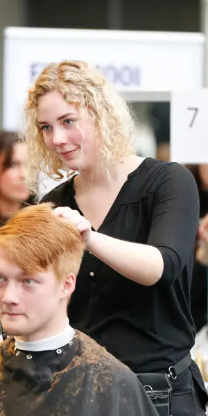 Leerling knipt en stylet een herenkapsel tijdens praktijkles uiterlijke verzorging in een kappersstudio