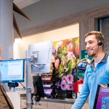 Medewerker helpt klant aan balie bij het afrekenen in een winkelomgeving met schermen en productpresentatie