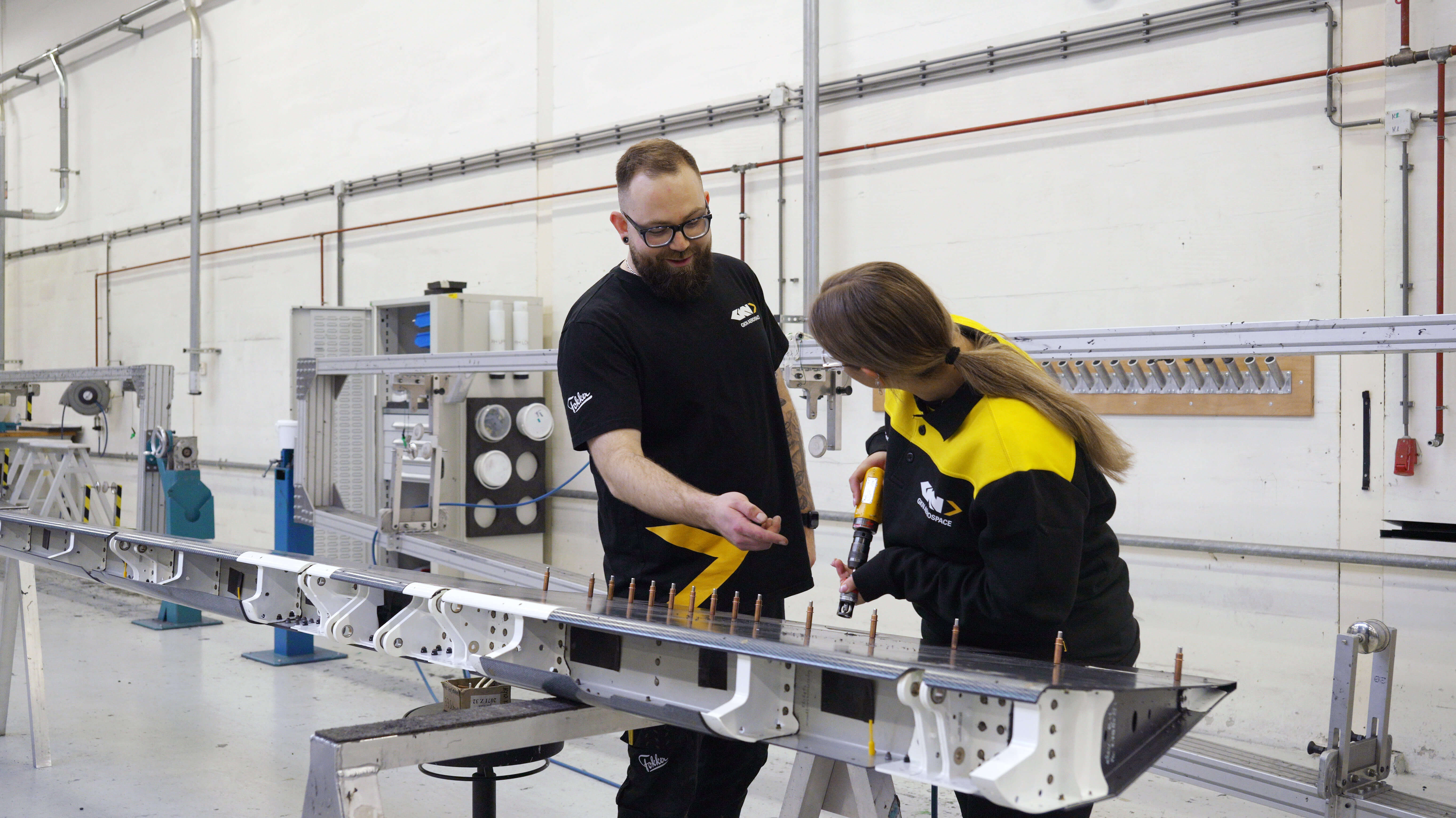 Technisch docent begeleidt student bij samenbouwen van vliegtuigonderdelen in werkplaats