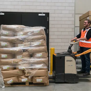 Logistiek teamleider bedient palletwagen om goederen te verplaatsen in een magazijnomgeving