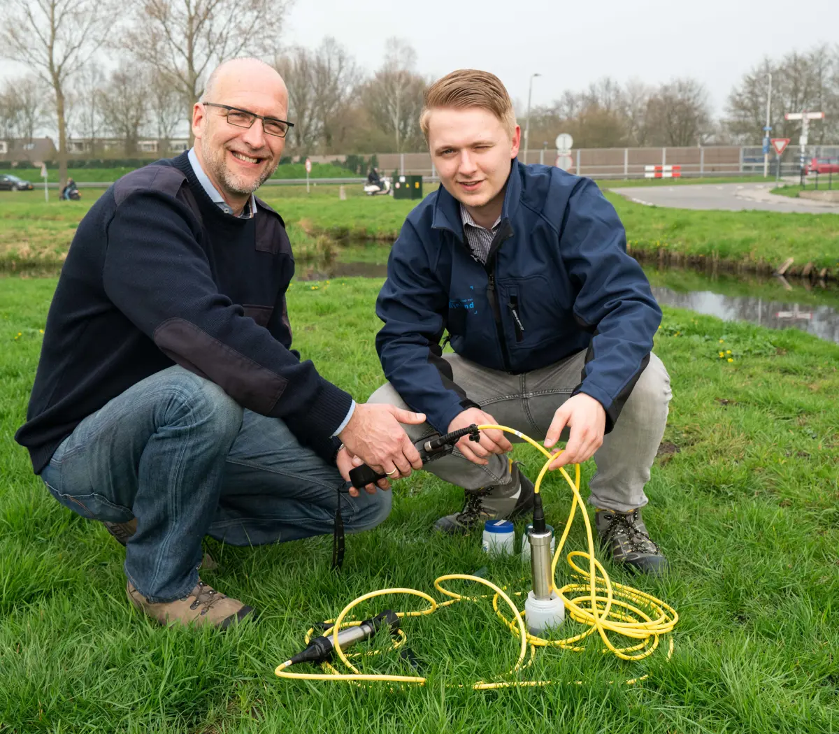 Adviseur leefomgeving test waterkwaliteit met meetinstrumenten in een grasveld nabij een waterloop