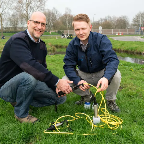 Adviseur leefomgeving test waterkwaliteit met meetinstrumenten in een grasveld nabij een waterloop