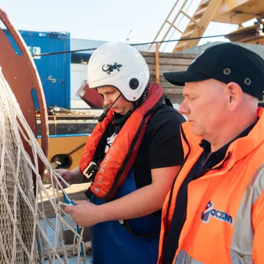 Een leerling volgt instructies van een schipper tijdens werkzaamheden aan boord van een vrachtschip