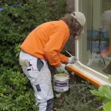 Gezel schilder brengt verf aan op houten kozijn, gespecialiseerd in afbouw en onderhoud