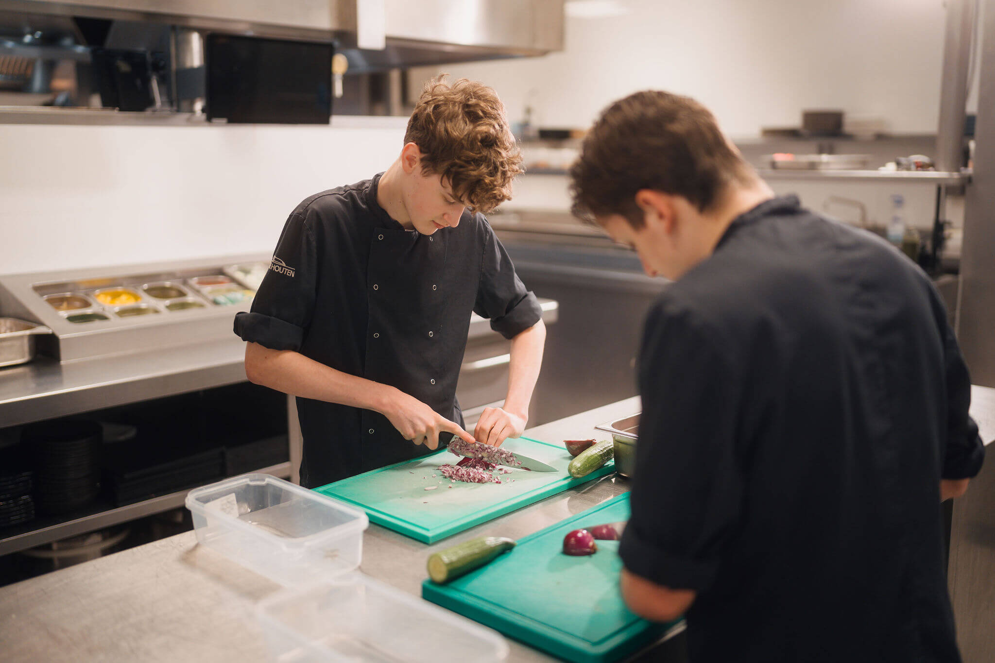 Koks in opleiding bereiden gesneden ingrediënten voor tijdens praktijkles in een professionele keuken.