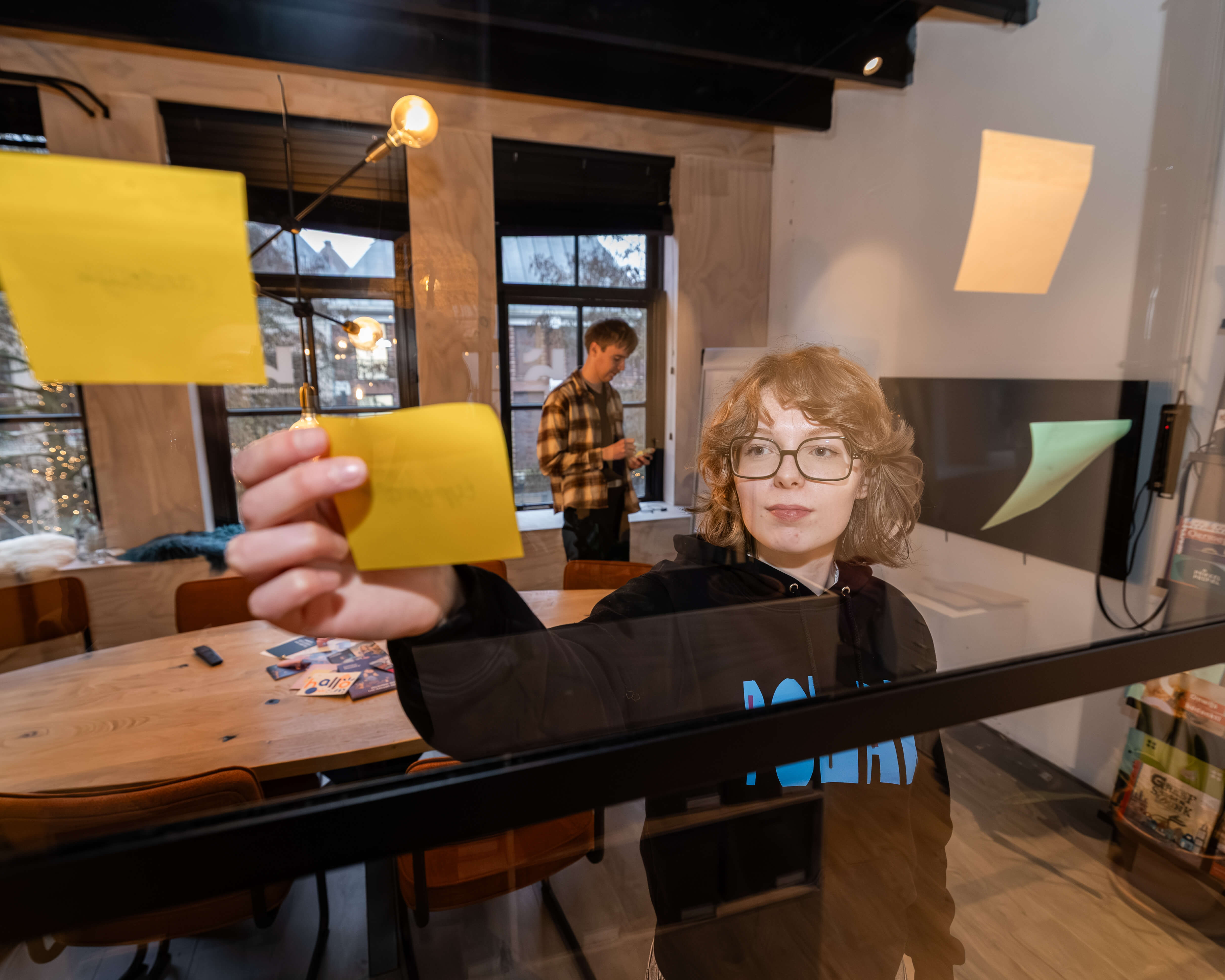 Mediavormgever plakt ideeën op een glazen wand tijdens het creatieve ontwerpproces