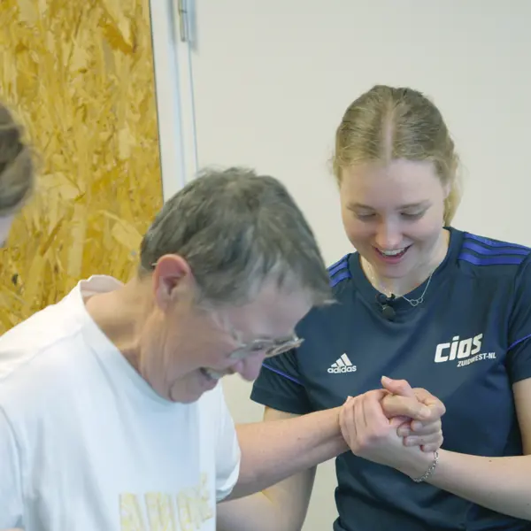 Docent begeleidt deelnemer bij oefening voor betere mobiliteit in praktijkruimte