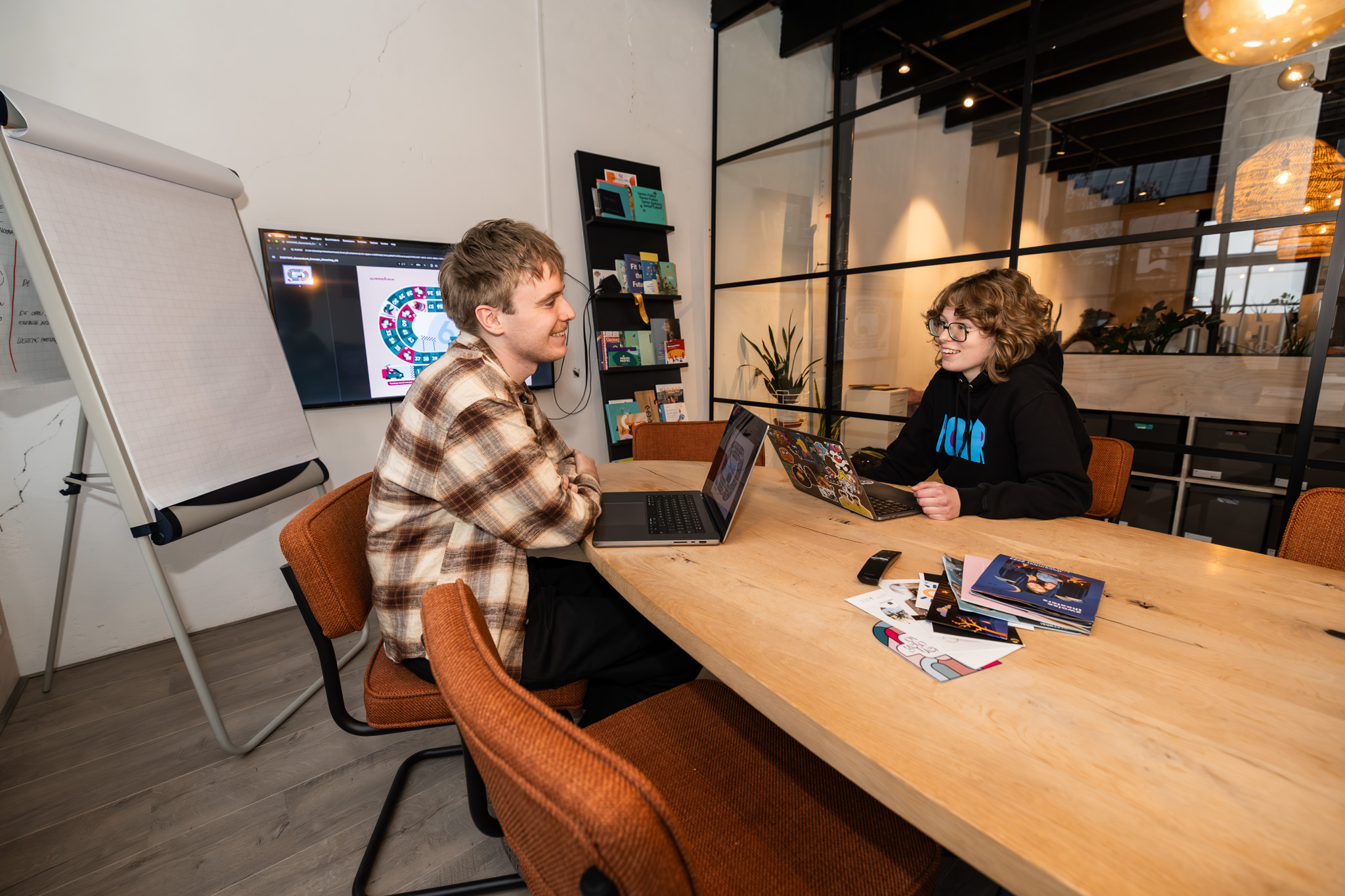 Twee studenten werken samen aan mediaprojecten met laptops in een leerzame werkomgeving.