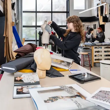 Student werkt aan een kledingstuk in een praktijkruimte voor modeontwerp en materialen.