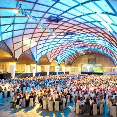 Een volle evenementenzaal waar organisator en deelnemers samen een conferentie bijwonen.