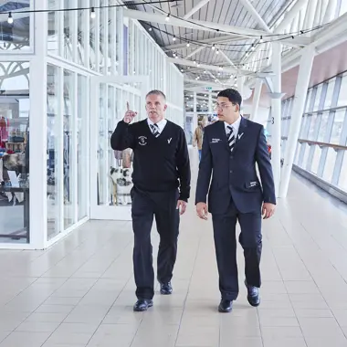 Twee beveiligingsmedewerkers lopen in een grote hal en bespreken taken voor het waarborgen van veiligheid.