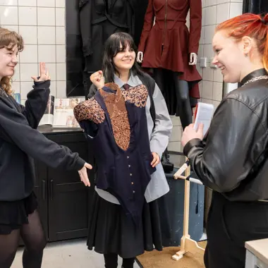 Drie jongeren bespreken een kledingontwerp in een modestudio tijdens een mbo-modeopleiding.