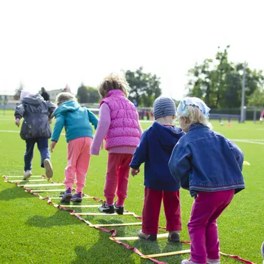 Begeleider helpt een groep kinderen tijdens een beweegactiviteit buiten op een sportveld.