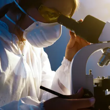Zorgprofessional onderzoekt monsters met microscoop, toont praktische en zorgzame kant van zorgberoepen.