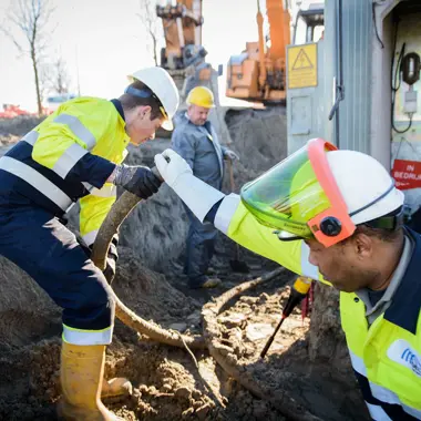 Technici installeren en beheren technische systemen in een buitengebied tijdens graafwerkzaamheden.