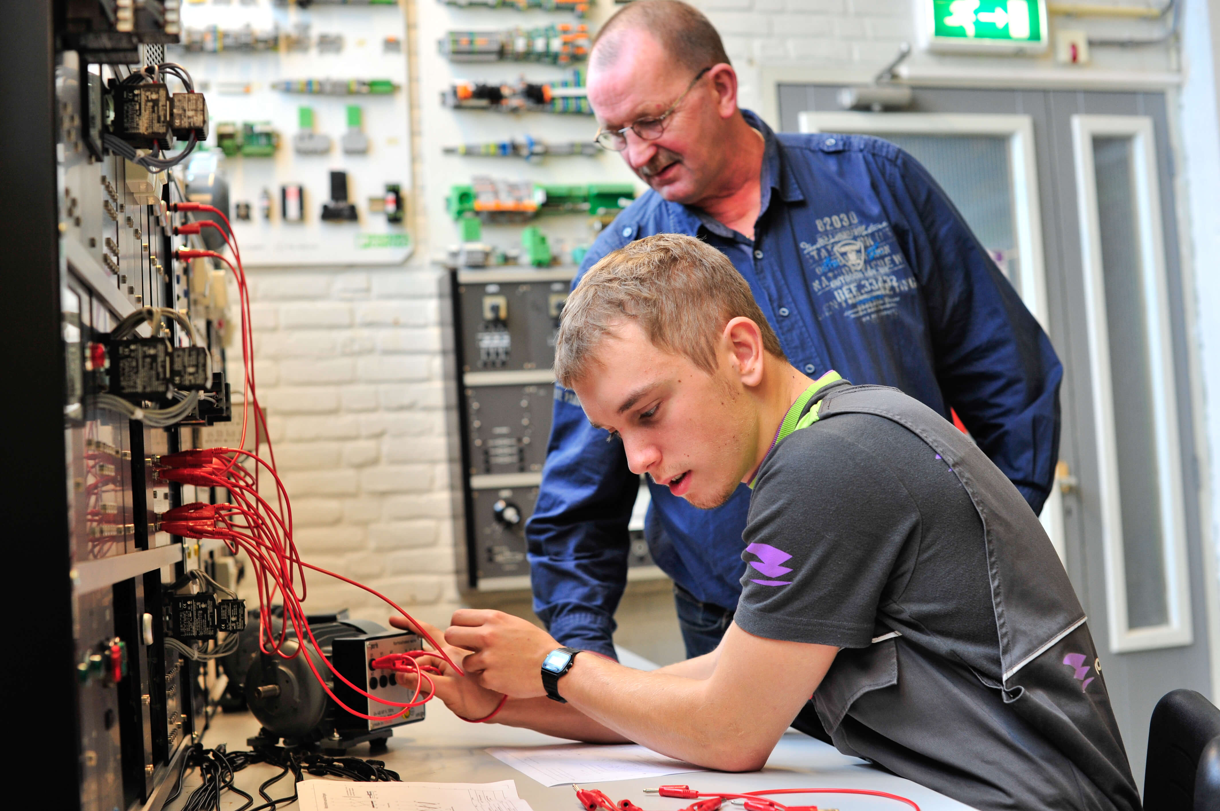 Jongere werkt geconcentreerd aan een elektrisch circuit tijdens een techniekles, begeleid door een instructeur.