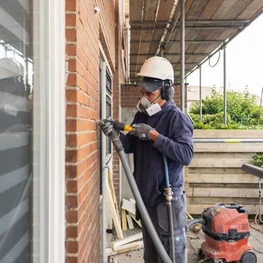 Vakbekwame bouwmedewerker gebruikt gereedschap voor werkzaamheden aan gevel tijdens renovatie