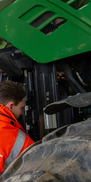 Medewerker groen, grond en groene infra controleert onderhoud aan landbouwmachine in werkplaats
