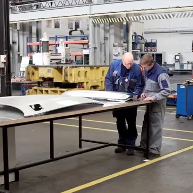 Twee vakmensen overleggen bij een metalen plaat in een industriële werkplaats voor metaalbewerking en montage.