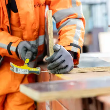 Vakman in oranje werkkleding gebruikt hamer voor het plaatsen van houten onderdelen bij infrastructuurwerk.