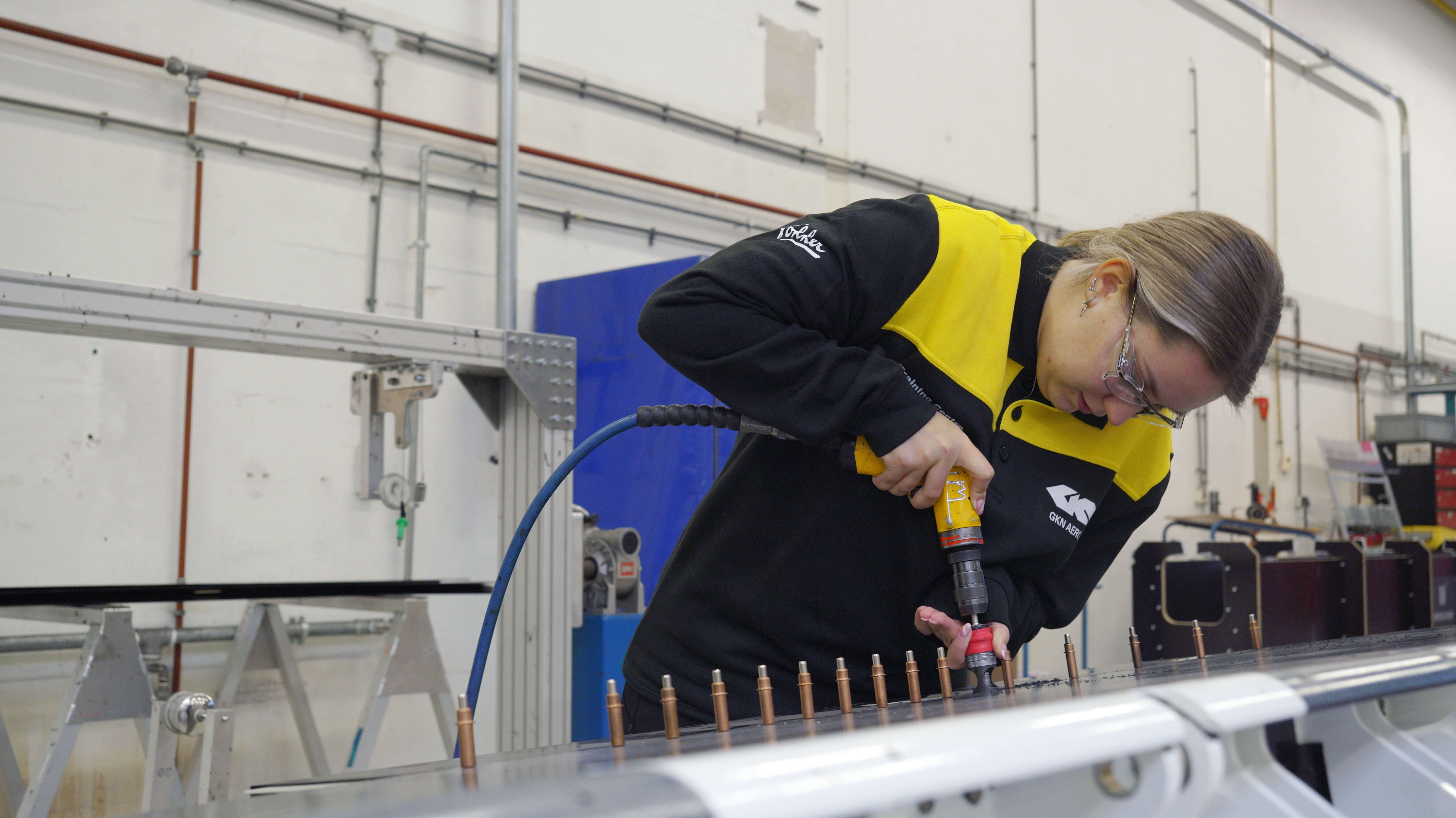 Student werkt geconcentreerd met pneumatisch gereedschap aan een metalen vliegtuigonderdeel in een werkplaats
